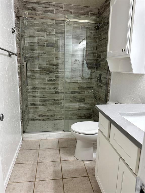 bathroom with vanity, toilet, a textured wall, a shower stall, and tile patterned floors