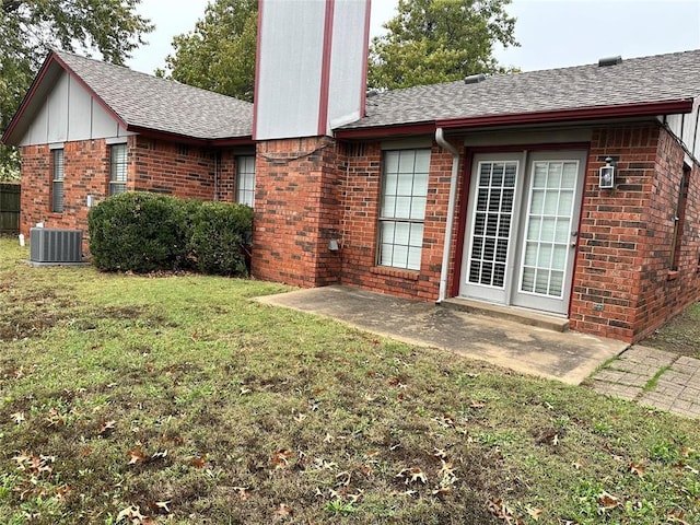 back of property featuring cooling unit, brick siding, roof with shingles, and a lawn