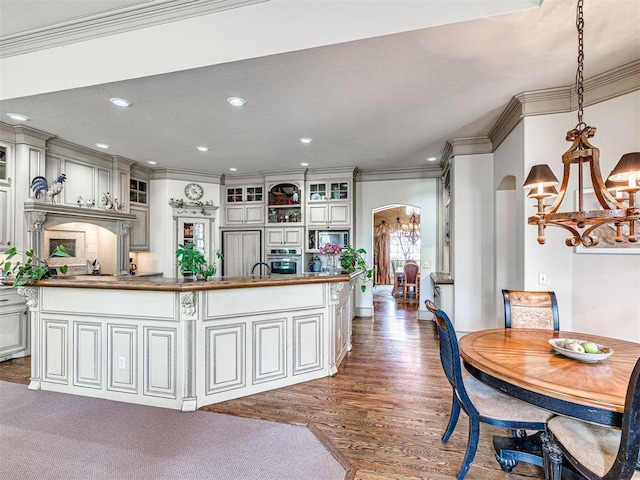 kitchen with crown molding, wood finished floors, an inviting chandelier, arched walkways, and oven