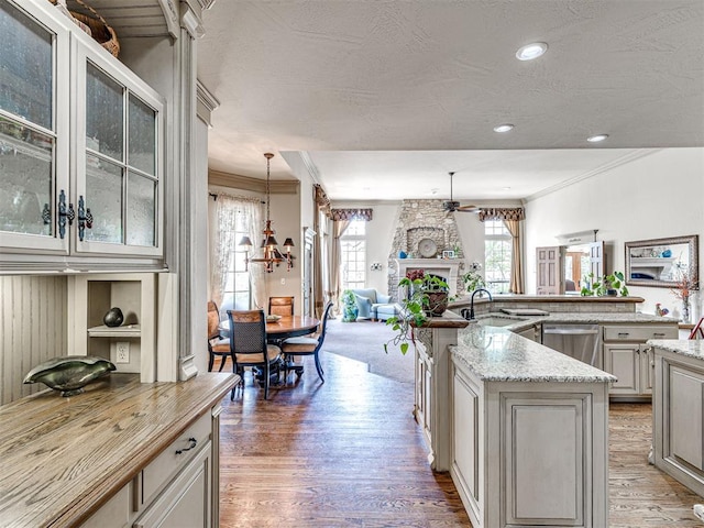 kitchen with a large fireplace, ornamental molding, ceiling fan with notable chandelier, open floor plan, and stainless steel dishwasher