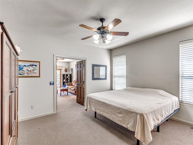 bedroom with light colored carpet, ceiling fan, baseboards, and a textured ceiling