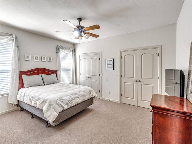 bedroom with light colored carpet, a textured ceiling, baseboards, and a ceiling fan