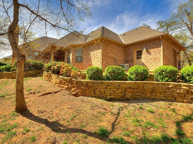 view of home's exterior featuring a shingled roof, central AC unit, and brick siding