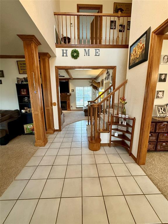 stairway with tile patterned flooring, ornate columns, carpet flooring, a high ceiling, and a fireplace