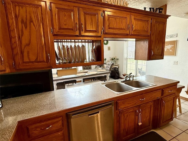kitchen featuring brown cabinets, a sink, a textured wall, stainless steel dishwasher, and light tile patterned floors