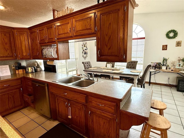 kitchen featuring a sink, backsplash, dishwasher, a textured ceiling, and light tile patterned floors