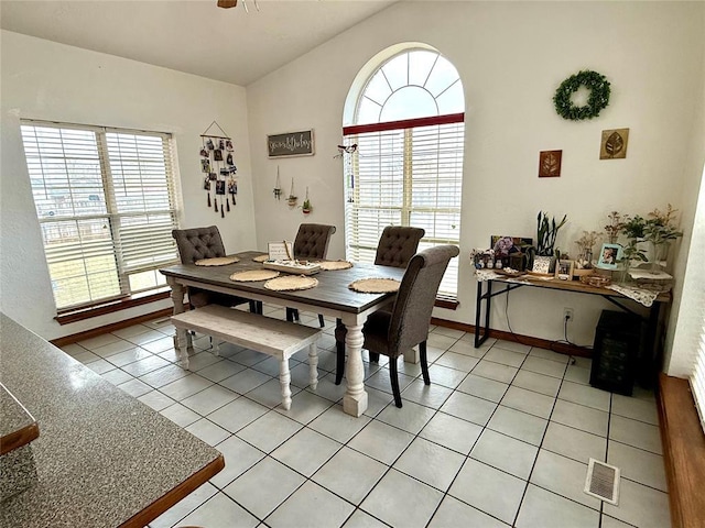 dining space featuring baseboards, visible vents, vaulted ceiling, and light tile patterned floors