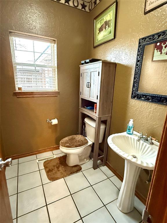 half bathroom with baseboards, toilet, tile patterned flooring, and a textured wall
