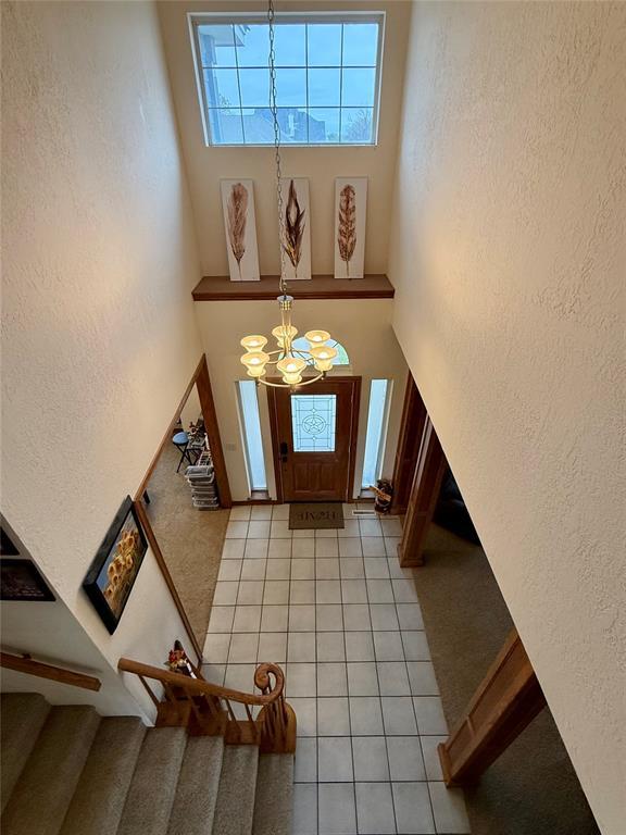 entryway with stairs, a textured wall, light tile patterned floors, and a chandelier