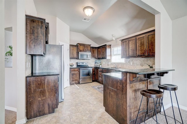kitchen with vaulted ceiling, a peninsula, dark brown cabinets, decorative backsplash, and stainless steel appliances