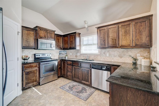 kitchen with appliances with stainless steel finishes, dark brown cabinetry, dark stone counters, lofted ceiling, and a sink