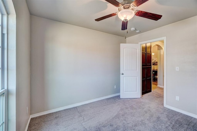 unfurnished bedroom with arched walkways, carpet, baseboards, and a ceiling fan