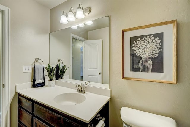 half bathroom with toilet, vanity, and a textured wall