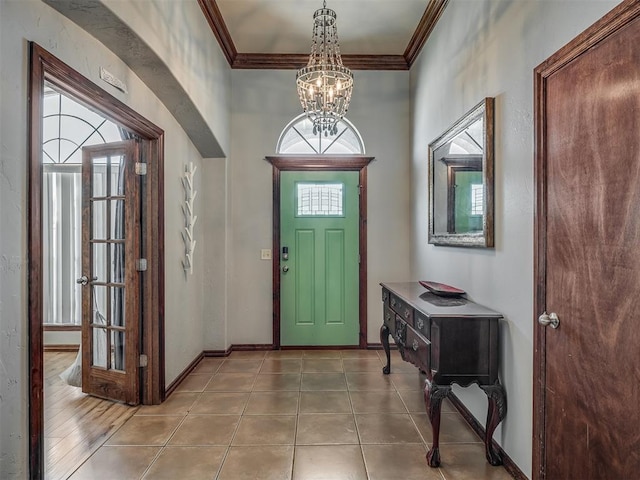 entryway featuring crown molding, tile patterned floors, baseboards, and a notable chandelier
