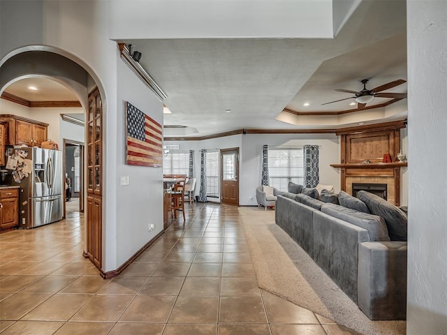 living area featuring light tile patterned floors, a tray ceiling, arched walkways, ornamental molding, and a ceiling fan