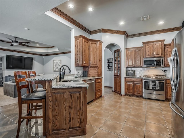 kitchen with a peninsula, a kitchen bar, a raised ceiling, arched walkways, and appliances with stainless steel finishes