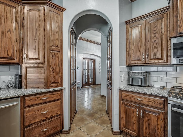 kitchen with light stone counters, light tile patterned flooring, decorative backsplash, stainless steel appliances, and arched walkways