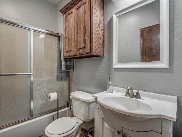 full bathroom featuring toilet, vanity, a textured wall, and bath / shower combo with glass door