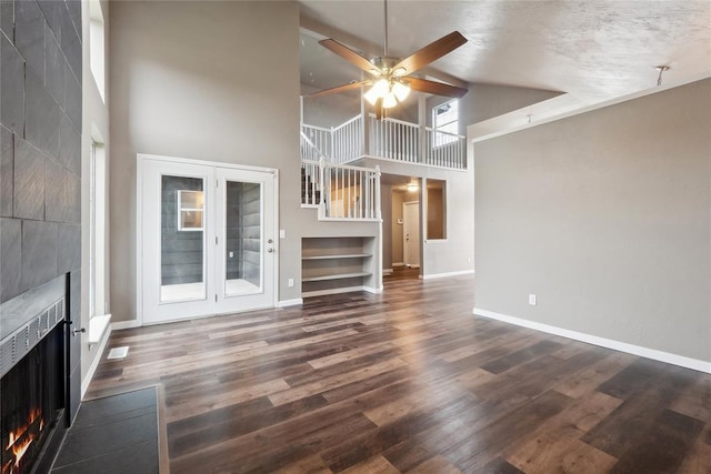 unfurnished living room with baseboards, wood finished floors, a large fireplace, ceiling fan, and high vaulted ceiling