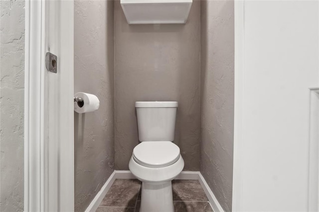 bathroom featuring baseboards, toilet, tile patterned flooring, and a textured wall