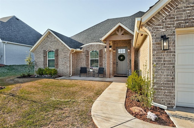 view of exterior entry featuring a lawn, a shingled roof, a garage, and brick siding