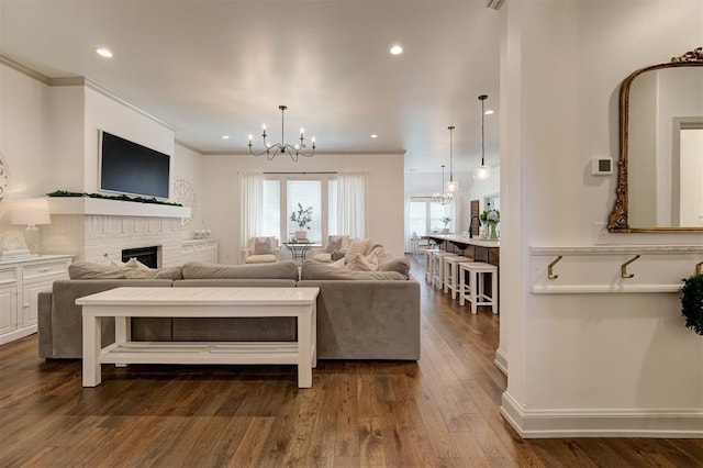 living area featuring crown molding, an inviting chandelier, recessed lighting, a brick fireplace, and dark wood-style floors