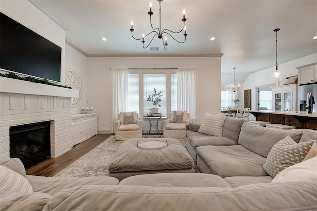living room with visible vents, a notable chandelier, a brick fireplace, crown molding, and wood finished floors