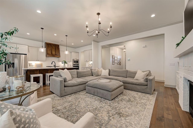 living room featuring dark wood-style flooring, recessed lighting, an inviting chandelier, and a brick fireplace