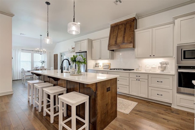 kitchen with a breakfast bar, appliances with stainless steel finishes, a kitchen island with sink, light countertops, and decorative backsplash