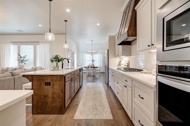kitchen with tasteful backsplash, custom exhaust hood, a sink, light countertops, and appliances with stainless steel finishes