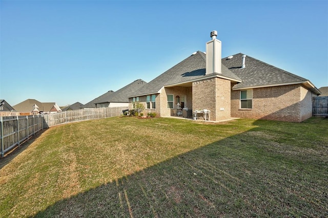 rear view of property with roof with shingles, a yard, brick siding, and a fenced backyard