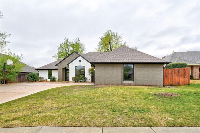 view of front facade with driveway, a front yard, roof with shingles, fence, and brick siding