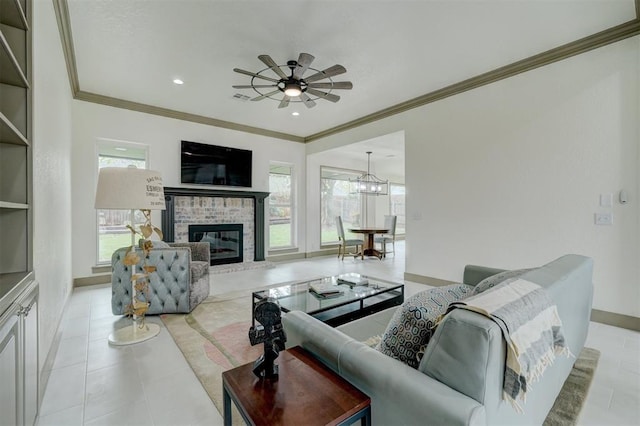 tiled living area featuring baseboards, ornamental molding, ceiling fan with notable chandelier, and a brick fireplace