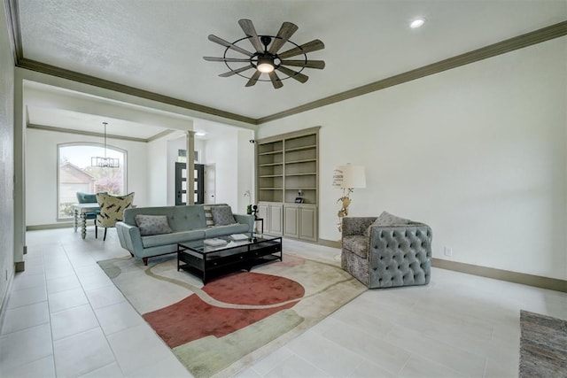 living area with decorative columns, tile patterned flooring, baseboards, ceiling fan with notable chandelier, and ornamental molding