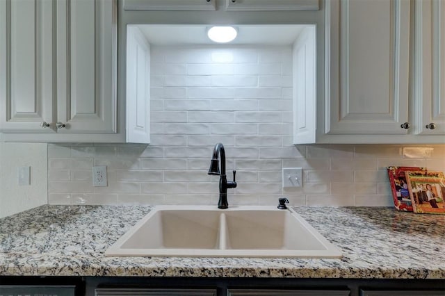 kitchen with light stone countertops, a sink, white cabinets, and tasteful backsplash