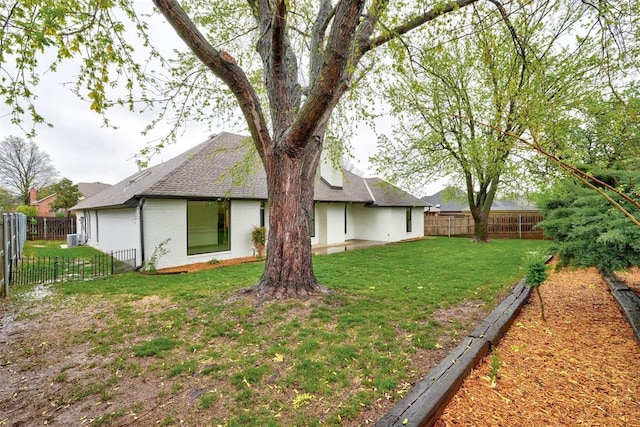 back of property featuring a garage, a fenced backyard, brick siding, a shingled roof, and a yard