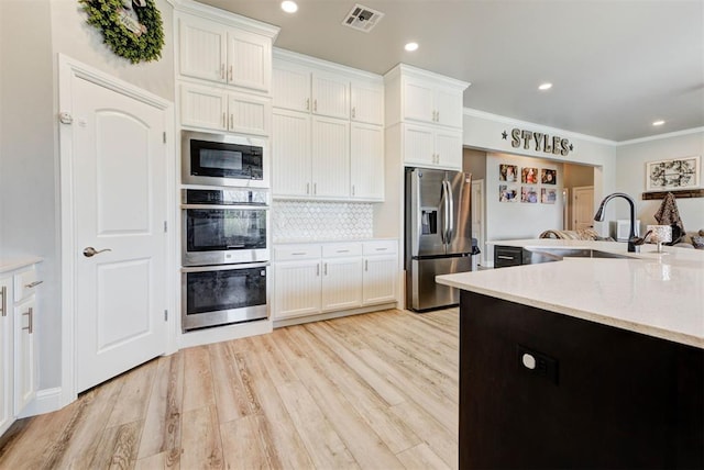 31352 Landrun Ave, Norman, OK 73072 - kitchen featuring stainless steel appliances, a sink, white cabinets, light wood-style flooring, and crown molding