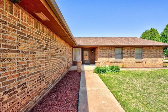 1809 W Aqua Clear Dr, Mustang, OK 73064 - view of exterior entry with a lawn, a shingled roof, and brick siding