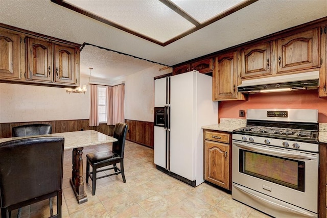 1809 W Aqua Clear Dr, Mustang, OK 73064 - kitchen featuring white refrigerator with ice dispenser, a textured ceiling, a wainscoted wall, under cabinet range hood, and stainless steel gas stove
