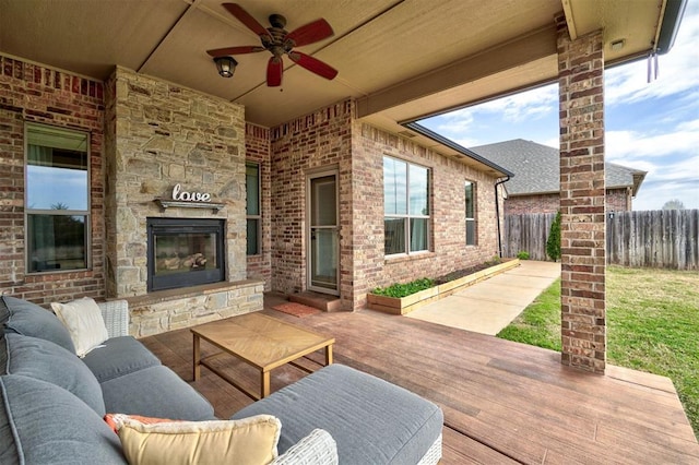 view of patio featuring an outdoor living space with a fireplace, fence, a wooden deck, and a ceiling fan