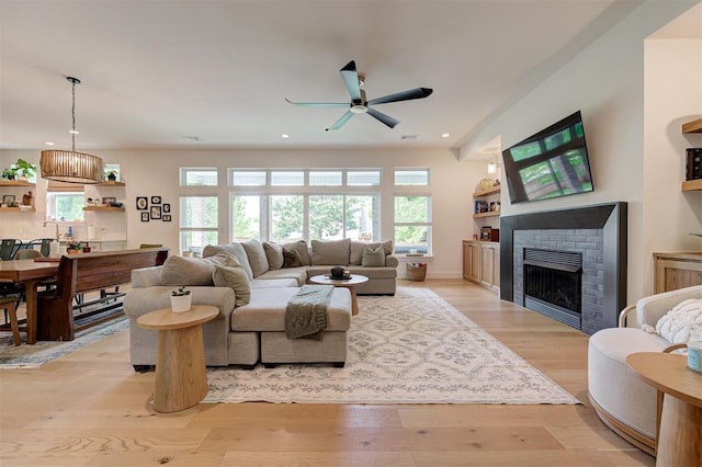 living room with a brick fireplace, light wood finished floors, ceiling fan, and plenty of natural light