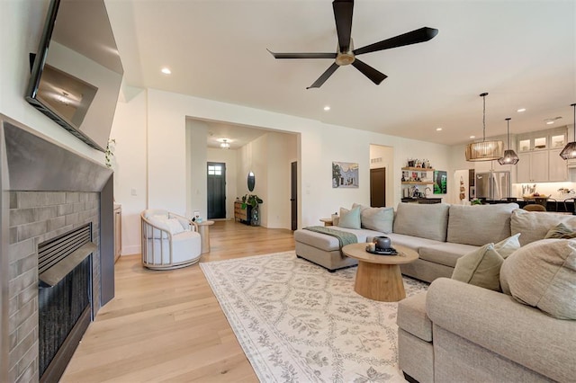 living room with a fireplace, a ceiling fan, light wood-style flooring, and recessed lighting