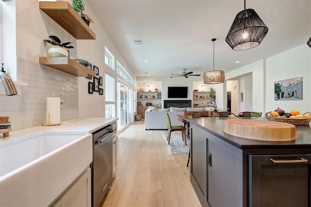 kitchen with a sink, open shelves, light wood-type flooring, a ceiling fan, and dishwasher