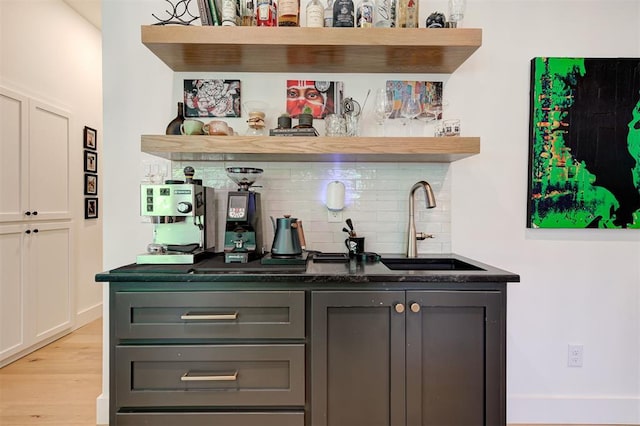 bar with a sink, light wood-type flooring, indoor wet bar, and backsplash