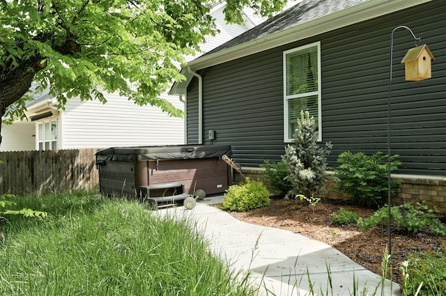 view of home's exterior with fence, a shingled roof, and a hot tub