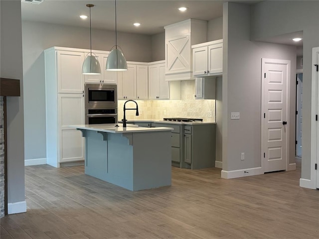 1220 SW 139th St, Oklahoma City, OK 73170 - kitchen with appliances with stainless steel finishes, backsplash, light wood-style flooring, light countertops, and a kitchen island with sink
