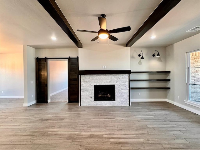 10116 NW 100th St, Yukon, OK 73099 - unfurnished living room with beamed ceiling, a ceiling fan, a barn door, wood finished floors, and a fireplace