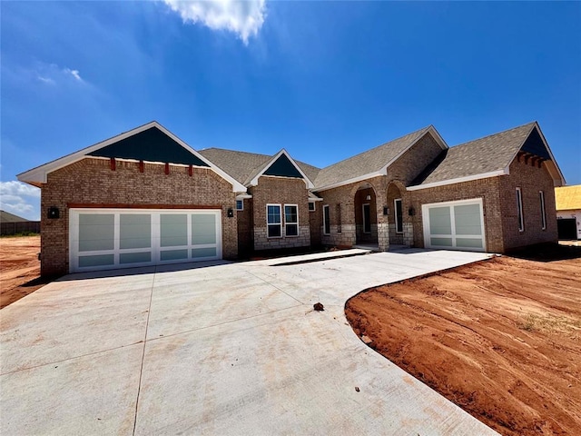 10132 NW 100th St, Yukon, OK 73099 - view of front of house featuring driveway, an attached garage, brick siding, and a shingled roof