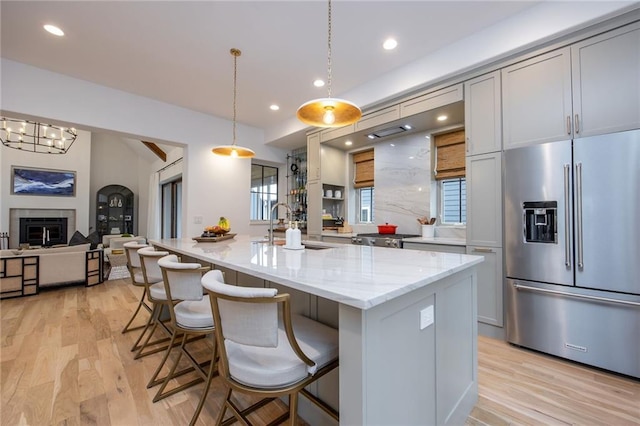 kitchen featuring a sink, light wood-type flooring, recessed lighting, light stone counters, and high end fridge
