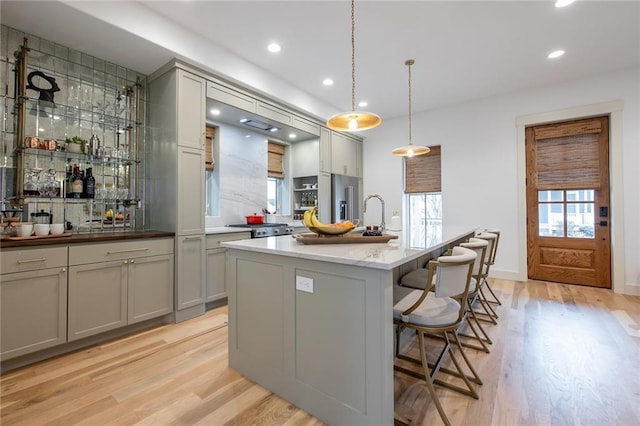 kitchen with light wood-type flooring, a kitchen breakfast bar, high quality fridge, and gray cabinets